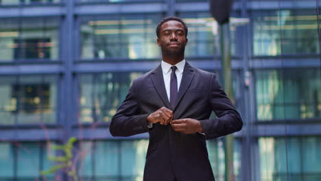 Portrait-Of-Confident-Young-Businessman-Fastening-Suit-Jacket-Standing-Outside-Offices-In-The-Financial-District-Of-The-City-Of-London-UK