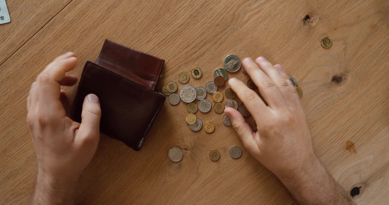 Vista superior de una persona vaciando monedas de una cartera sobre una mesa de madera. Concepto financiero de ahorros, presupuesto, cambio suelto, gastos y finanzas personales.
