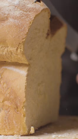 Vertical-Video-Close-Up-Of-Person-Cutting-Slices-Of-Fresh-Bread-From-Loaf