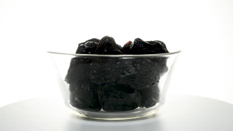 transparent glass bowl with dried plums rotating on a white background