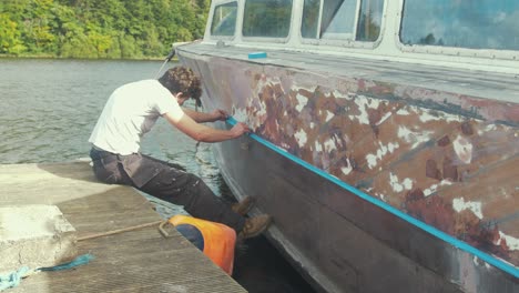 white male painter applying masking tape on rubbing strake of old wooden boat