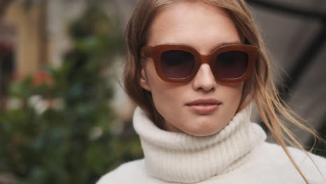 caucasian female wearing sunglasses and sweater outdoors.