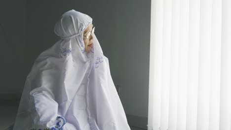 elderly muslim woman praying alone near window