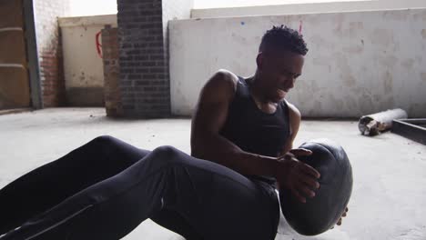 hombre afroamericano haciendo ejercicio con una pelota de medicina en un edificio urbano vacío