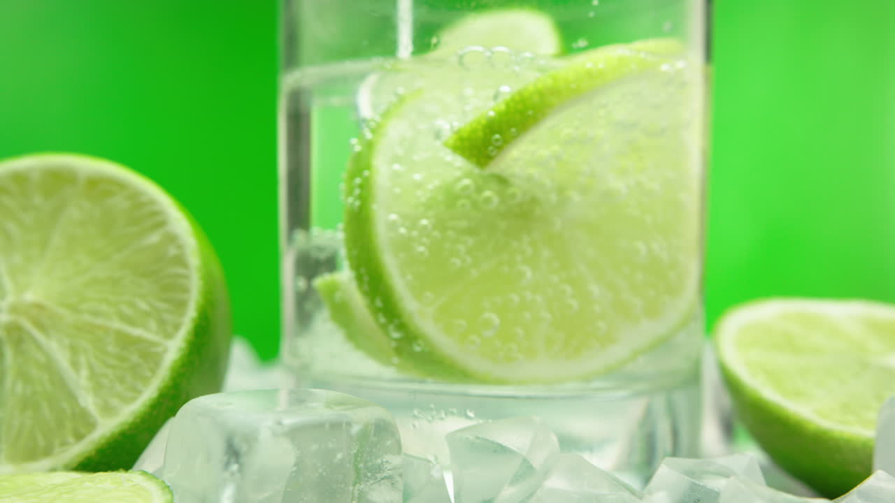 녹색 배경에 격리된 상쾌한 진 토닉, 녹색 레몬 및 얼음 블록이 포함된 알코올성 여름 음료의 클로즈업 제품 비디오