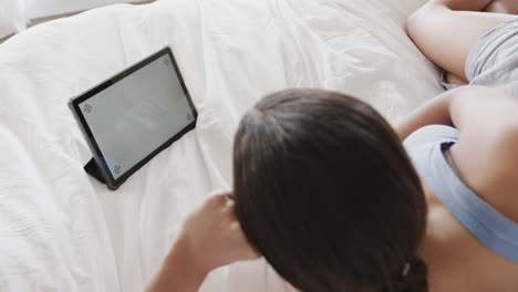 biracial woman lying on bed using tablet with copy space on screen, slow motion