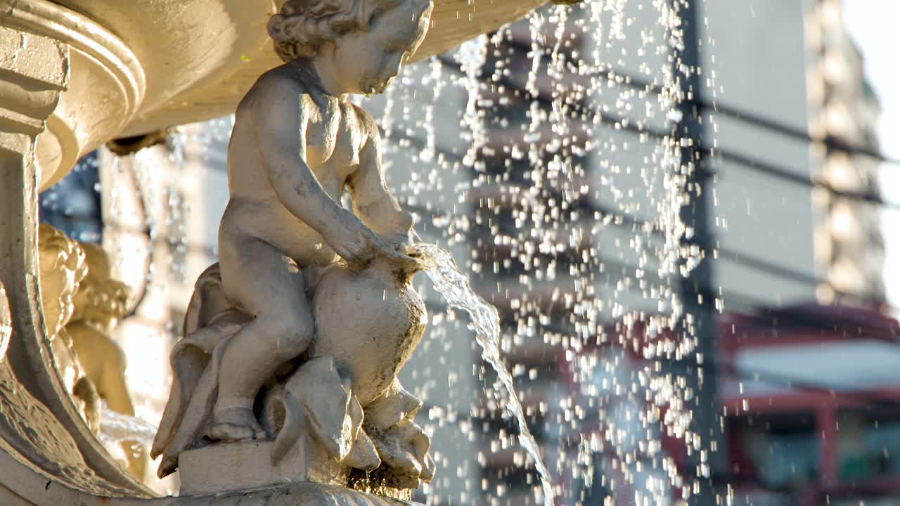 Sunlight illuminates a stone cherub statue as water splashes from a fountain in Manila