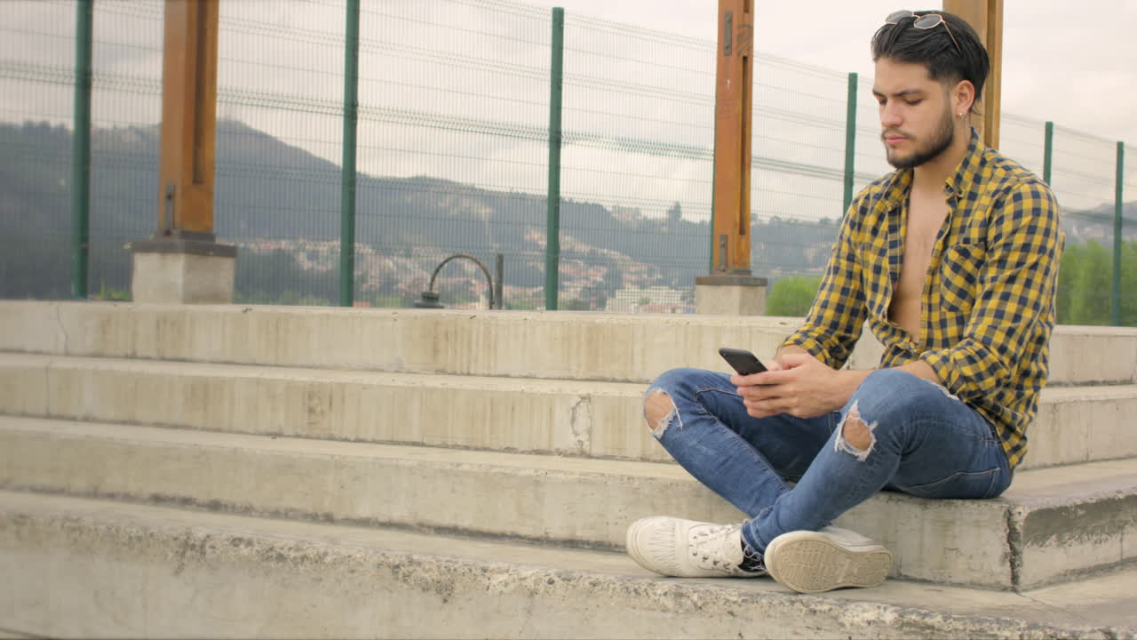 chico guapo sentado en las escaleras trabajando en su computadora portátil y teléfono celular