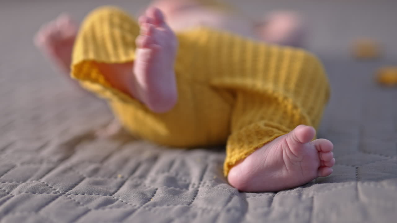 Small kid in yellow pants lying on the bed with his tiny feet to the camera. Beautiful little baby feet close up.