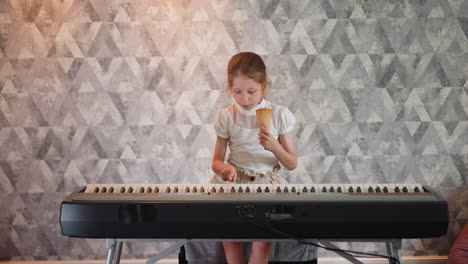 young girl in white top sitting indoors, holding ice cream cone while learning to play keyboard piano, focused expression on face, against modern geometric patterned wall