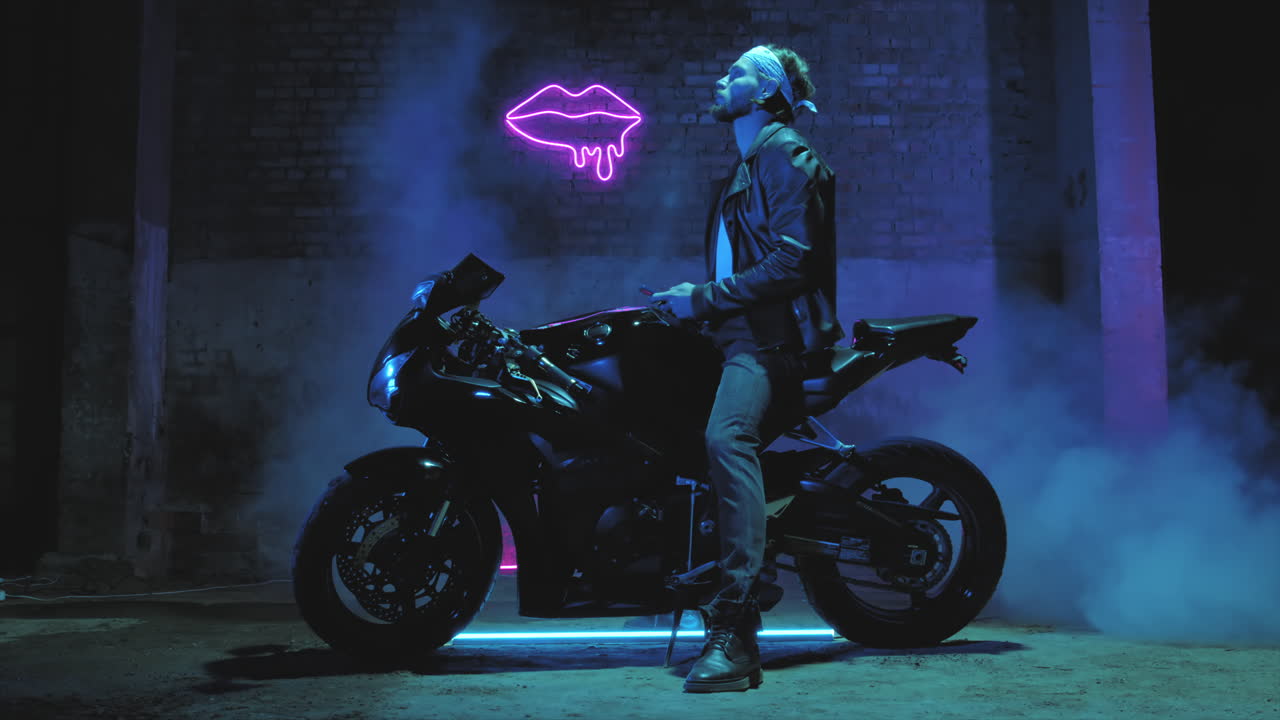 반다마 를 입은 남자 가 스포츠 오토바이 에 앉아서 벽돌 벽 에 맞서 휴대 전화 로 문자 를 보내고 있다