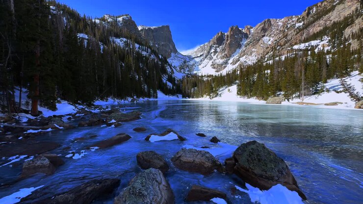 Paesaggio invernale del Lago dei Sogni con ghiaccio limpido, blu intenso e congelato nel Parco Nazionale delle Montagne Rocciose (RMNP), Colorado. Vista aerea da drone del Lago Smeraldo in alta montagna, sentiero del Bear Lake, con il picco Hallett sotto un cielo azzurro e soleggiato e le Montagne Flattop.