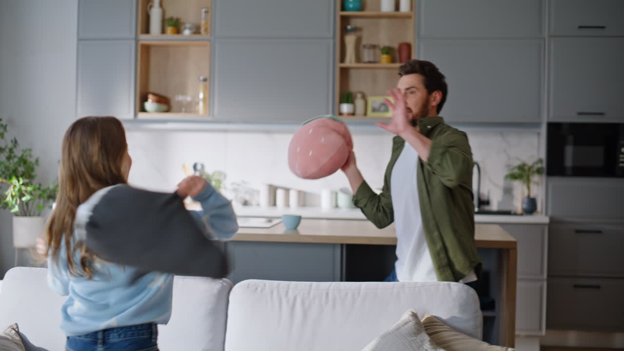 Happy father playing girl funny game home. Smiling man fighting pillows daughter