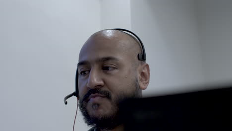 A-close-up-shot-of-an-Asian-help-desk-employee-talking-to-a-customer-through-a-microphone-headset,-the-man-deeply-entrenched-in-his-conversation