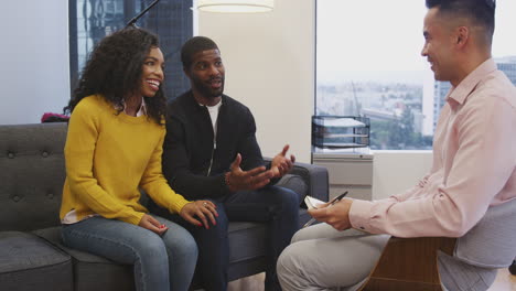 casal sentado no sofá reunindo-se com um conselheiro masculino no escritório
