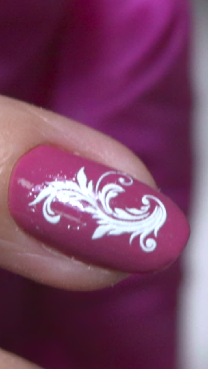 Primo piano: Mano caucasica con guanto rosa mostra smalto color malva con decalcomania a spirale bianca ornata, manicurista che tiene. Media