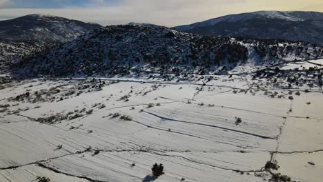 Vuelo-Lateral-Con-Dron-Sobre-La-Ladera-De-Una-Montaña-Con-Una-Gran-Nevada-En-La-Zona-Creando-Un-Efecto-De-Paralaje-Con-Un-Sistema-Montañoso-Ubicado-Detrás-De-La-Montaña-Con-Un-Cielo-Blanco,-ávila,-España