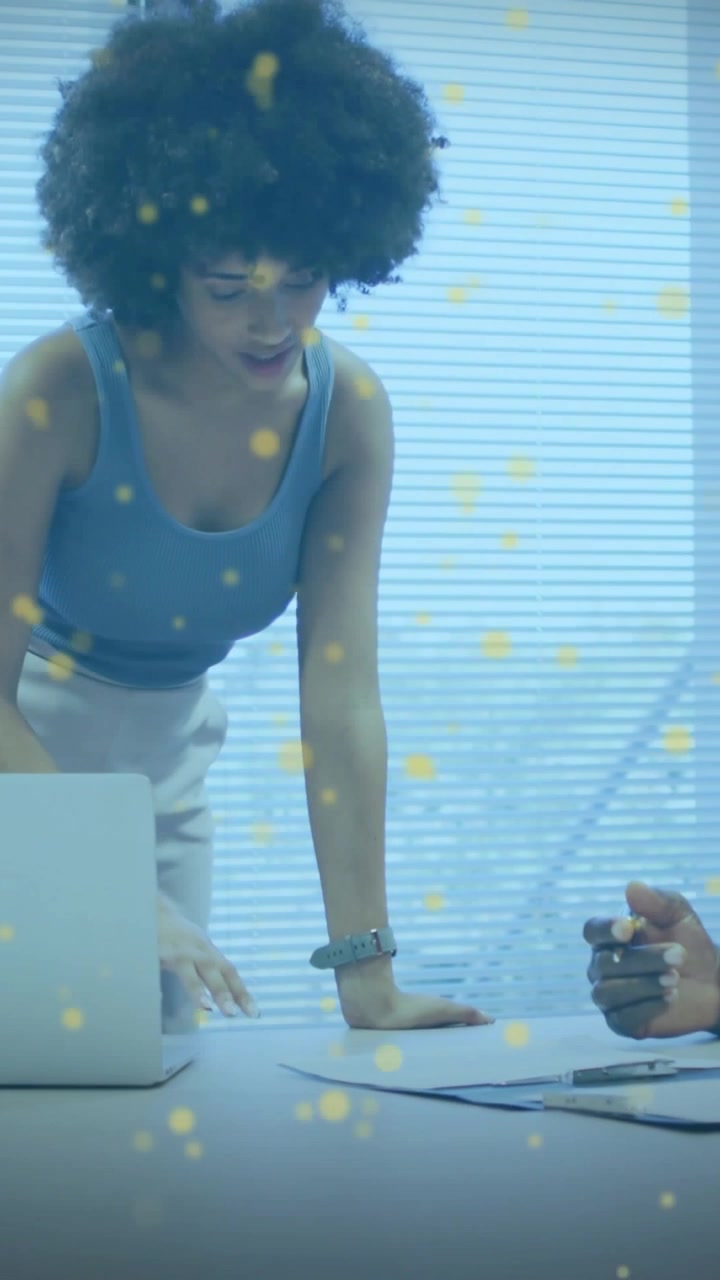 Woman leaning over table reviewing docs, explaining biz as senior pointing pen, yellow dots overlay