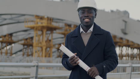 smiling engineer with plans at construction site