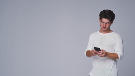 Studio-Shot-Of-Man-Against-White-Background-Sending-Text-Message-On-Mobile-Phone-In-Slow-Motion