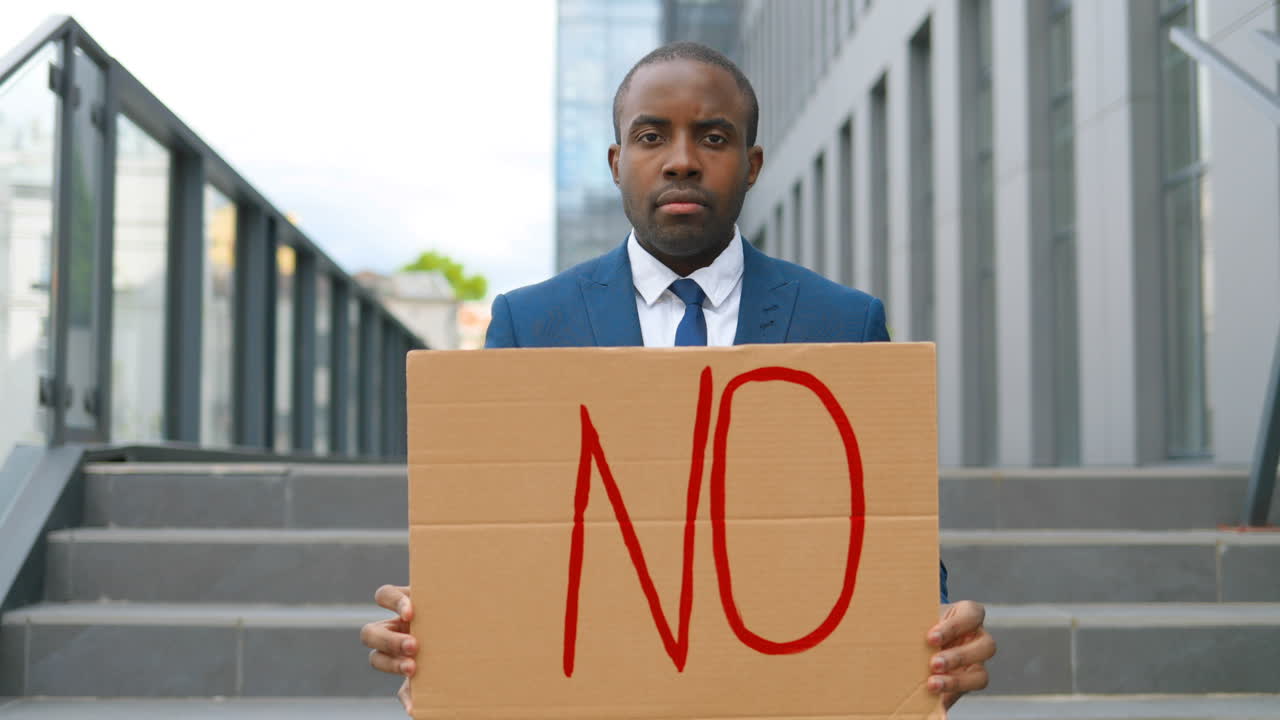 Portrait of african american elegant young man in blue suit showing No" signboard in the street"