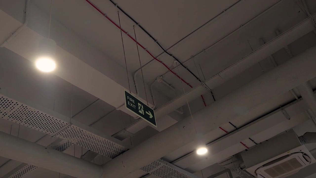 Interior shot of fire exit signage suspended from ceiling in modern office, mall, hospital or commercial building. Ideal for safety, emergency evacuation, compliance and facility management concepts.