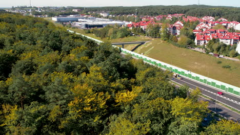 Drone-flyover-above-forest-reveals-highway-below-suburban-development,-Gdynia-Wielki-Kack-Poland