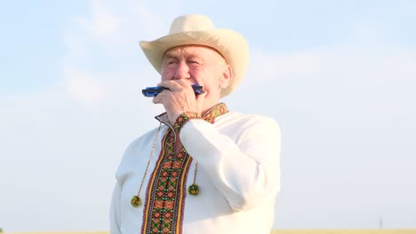 elderly man in traditional ukrainian shirt and cowboy hat playing harmonica