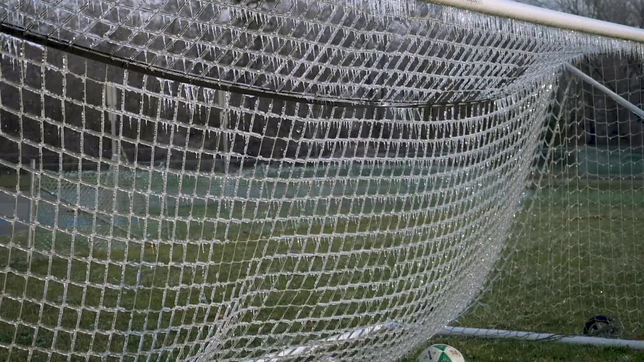 ZEITLUPE: Ein Fußball schlägt in ein vereistes Fußballtornetz ein, wobei zersplittertes Eis in die Luft fliegt.