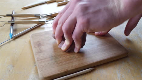 close up on the hands of an artist sculpting and shaping brown modeling clay with tools on the wooden table in a messy art studio