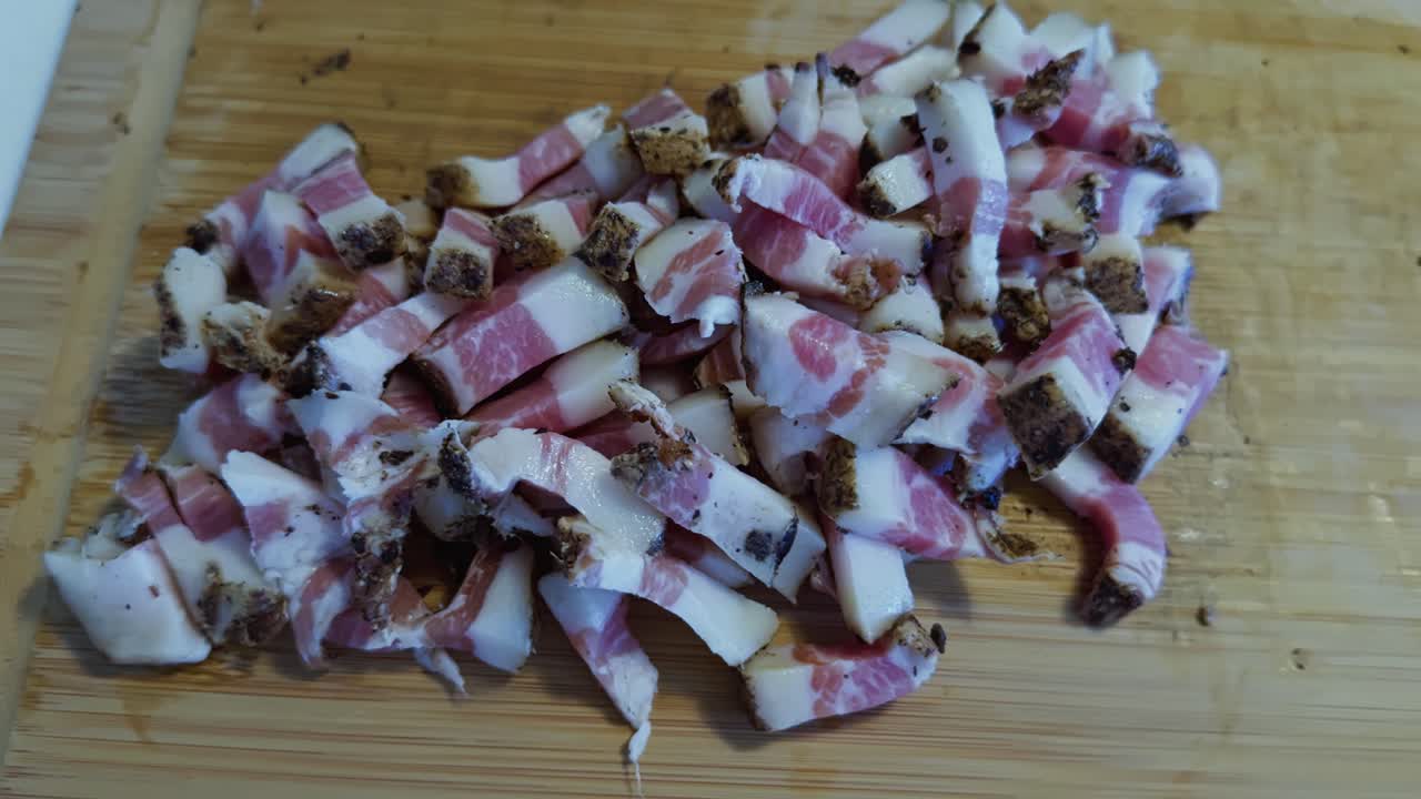 Orbiting closeup of diced guanciale pieces on wooden cutting board in natural kitchen light