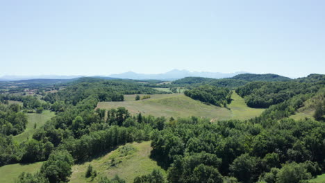 aerial boom shot showing the wild countryside with green forests and mountains on the horizon, bright summers day