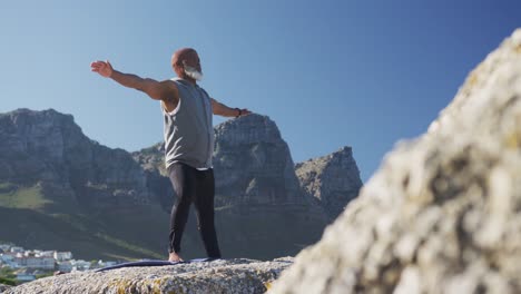 senior african american man exercising stretching on rocks by the sea