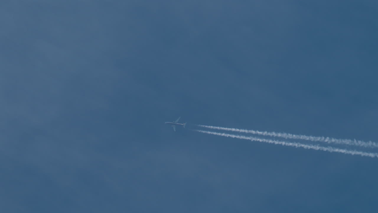 Airplane flying high above leaving long contrails in a clear blue sky