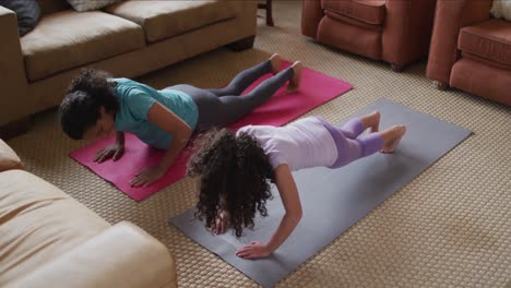 mixed race mother and daughter practicing yoga in living room