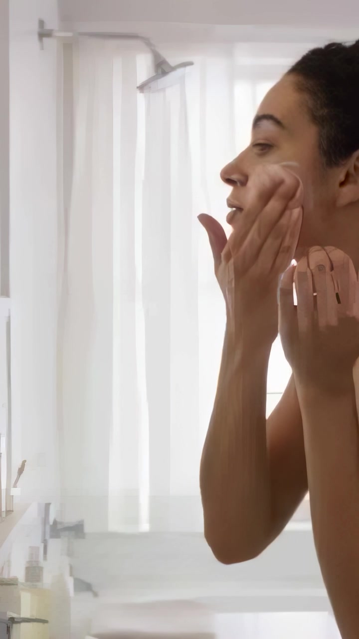 Vertical video: Applying foam lady in tank rubbing face at bath mirror by window, jars, copy space