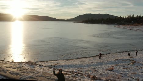 Fast-flyover-of-waving-woman-silhouetted-on-pier-towards-frozen-lake-at-sunset-hour