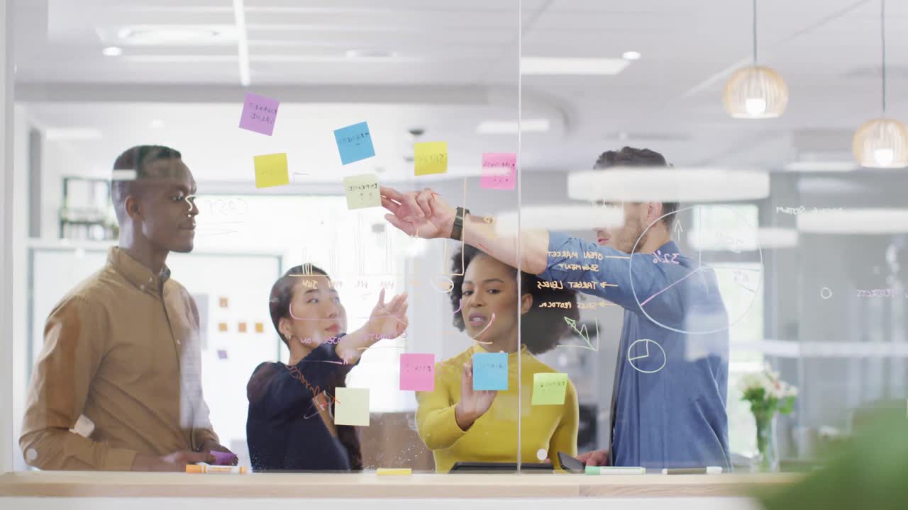 Diverse business people writing on glass blackboard and brainstorming at office, slow motion