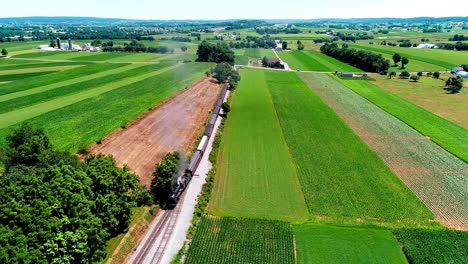 Steam-Train-Passing-through-Amish-Farm-Lands-and-Countryside-on-a-Sunny-Summer-Day-as-seen-by-Drone
