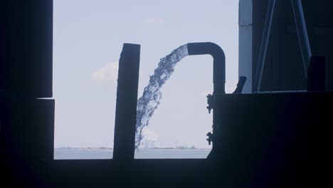 Große-Menge-Wasser,-Die-Aus-Einem-Rohr-In-Einer-Fischfabrik-In-Silhouetten-Zeitlupe-Gesprüht-Wird