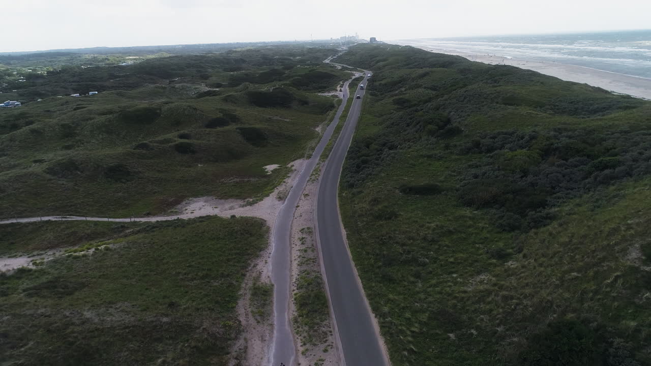 Drone vola sopra una strada costiera tra dune e mare in Spagna.