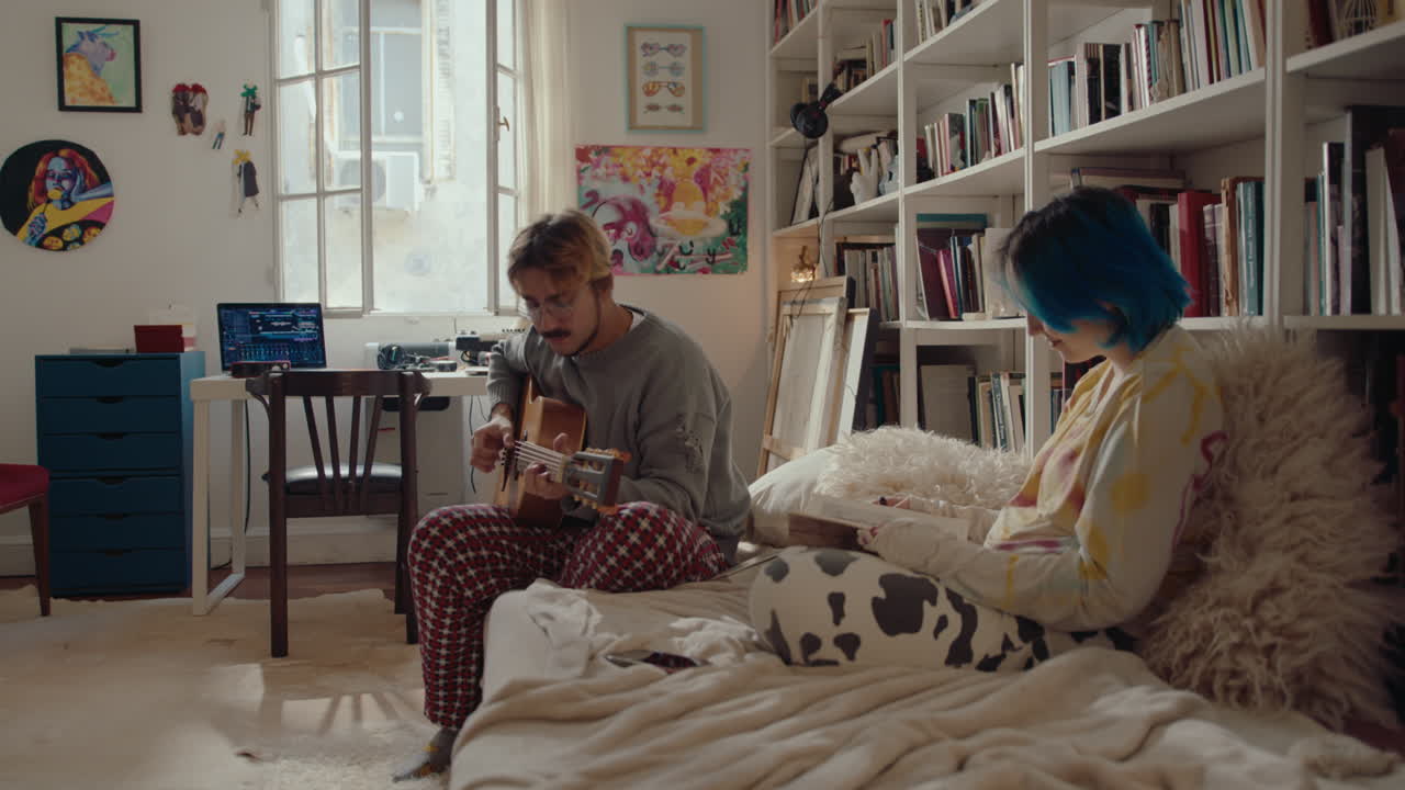 Young Man Playing the Guitar, Girlfriend Reading Book at Home