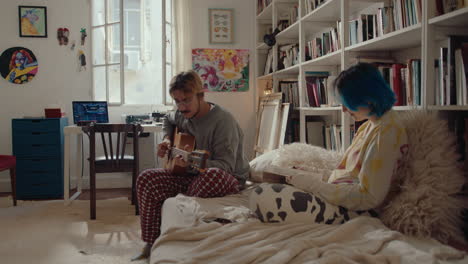 young man playing the guitar, girlfriend reading book at home