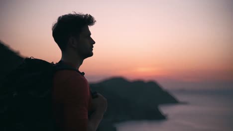 a young boy with backpack standing alone watching sunset along the mountain and sea
