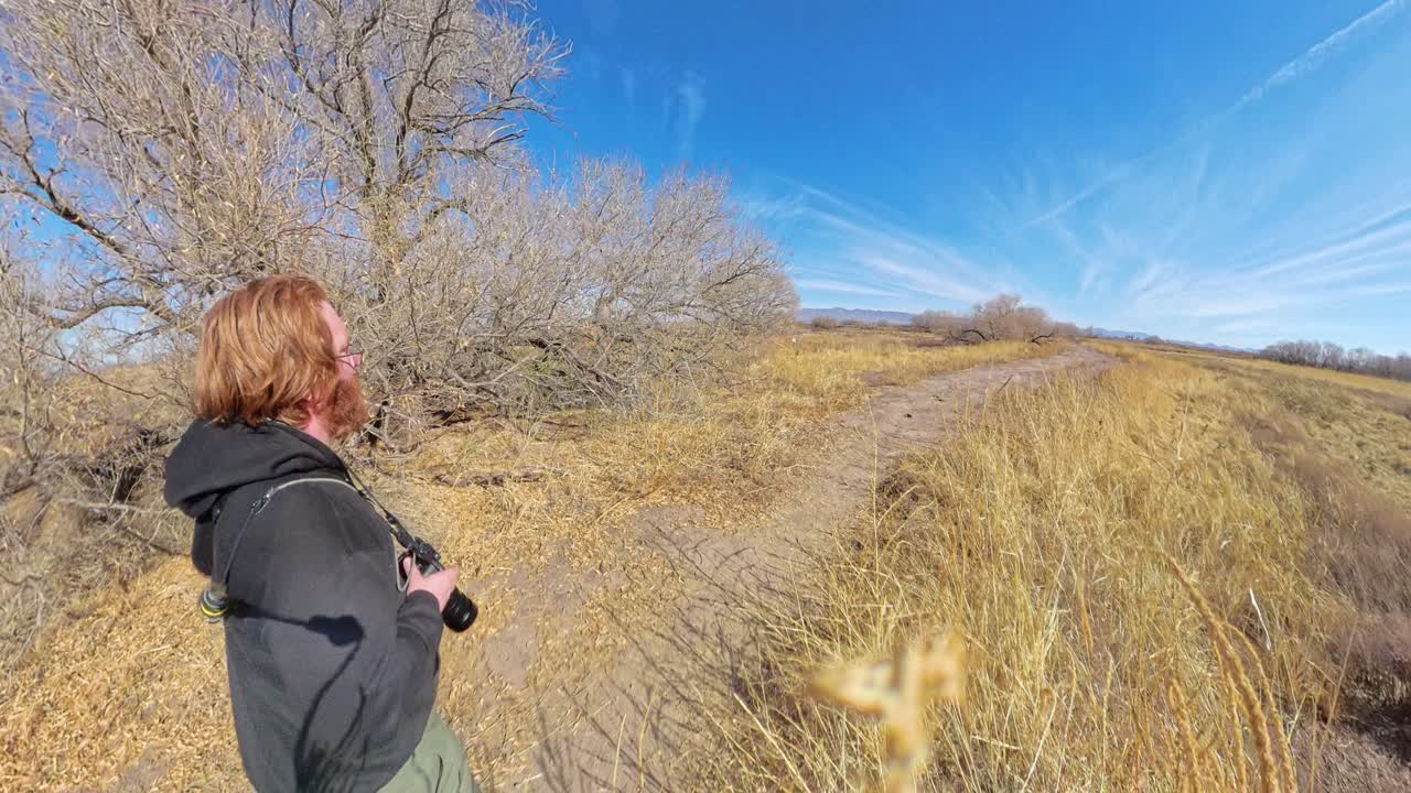Photographer walking through dry desert grassland in Arizona midday blue sky.