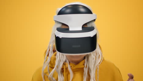 smiling old woman watching film in vr glasses on yellow studio background.