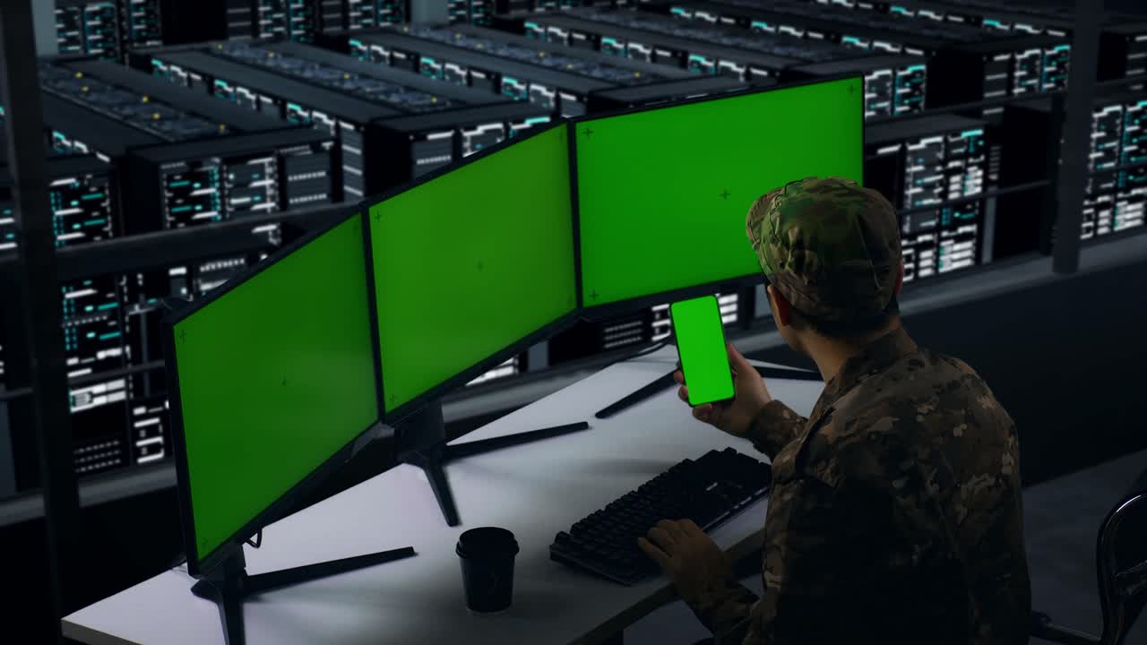 Side View Of Asian Military Using Mobile Phone And Multiple Computer Monitor With Mock Up Green Screen In Data Center