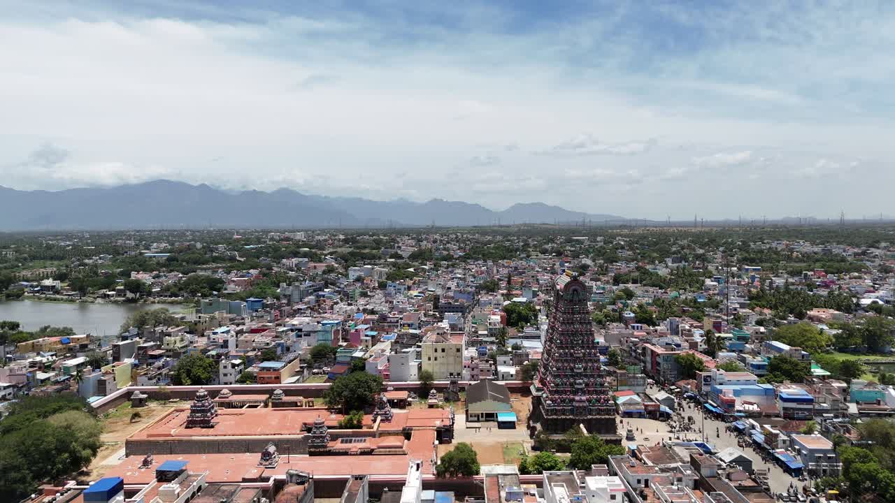 Drone video of Tenkasi’s historic Kasi Viswanathar Temple surrounded by colorful town buildings, a lake, and the scenic Western Ghats in the background. mix of modern and traditional buildings