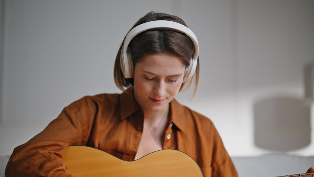 Headphones woman playing guitar at home closeup. Relaxed girl musician strumming