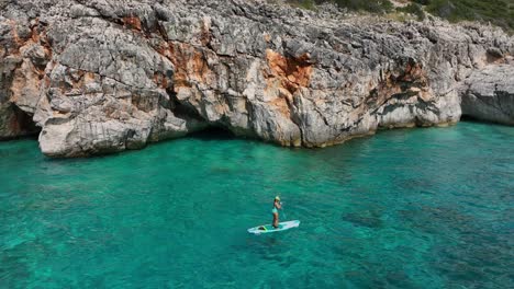 a woman paddle boarding on the beautiful turquoise coast of gjipe, albania.